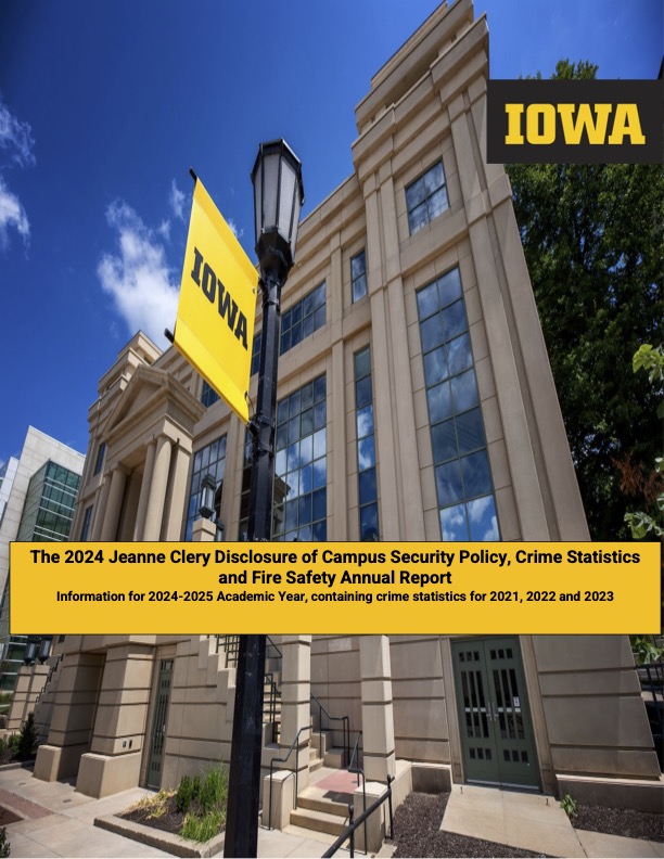 A vibrant photograph featuring a tall, beige building with large windows under a clear blue sky. In the foreground, there’s a black lamp post with two yellow banners hanging from it, both with ‘IOWA’ written in black letters. The top banner also includes additional text about the Jeanne Clery Disclosure of Campus Security Policy and Crime Statistics Report for the academic years 2024-2025, containing crime statistics for 2021, 2022, and 2023.