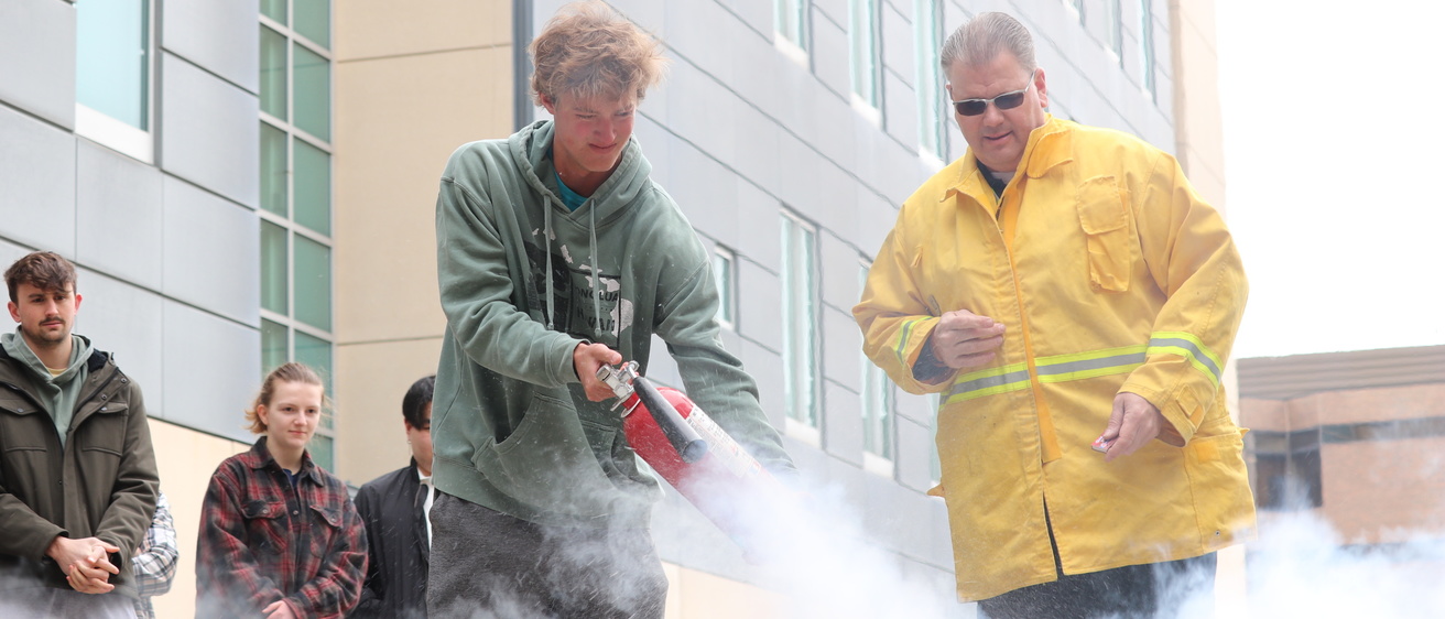 A student uses a fire extinguisher during a fire safety training session.